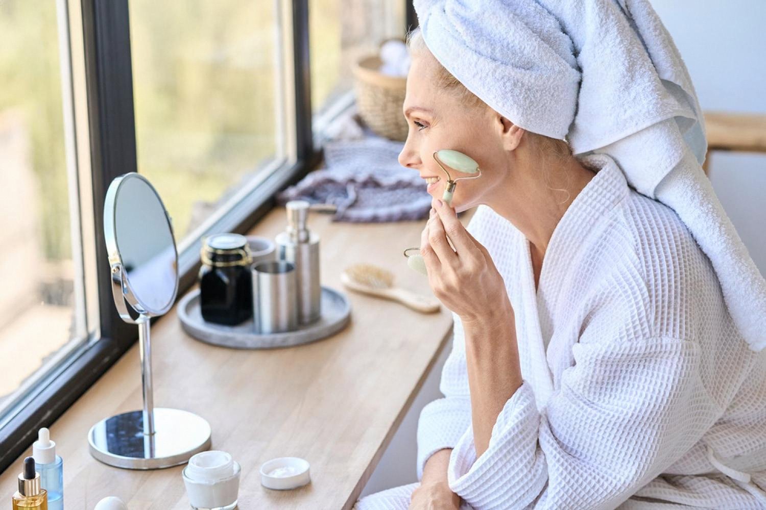 Woman in a white robe using a jade roller as part of her home skincare routine after an aesthetic treatment